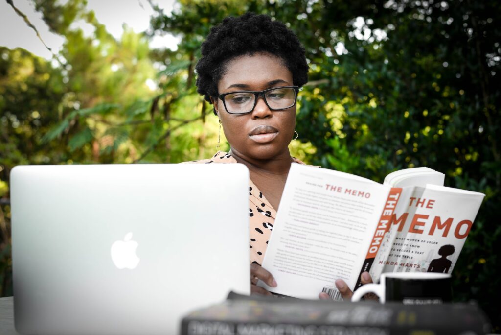 woman reading a book while working on a computer